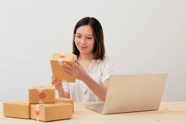 Mutlu Asyalı kadın karton kutuyla ev ambalajlama ve yazma sırası ile çalışıyor, online pazarlama paketleme ve teslimat, KOBİ kavramı
