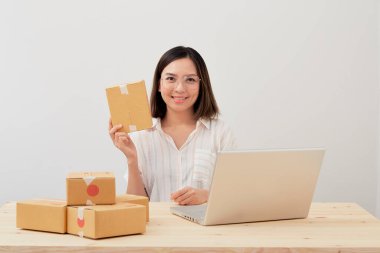 Mutlu Asyalı kadın karton kutuyla ev ambalajlama ve yazma sırası ile çalışıyor, online pazarlama paketleme ve teslimat, KOBİ kavramı