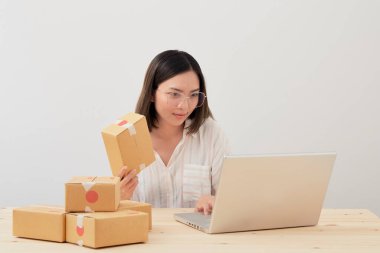 Mutlu Asyalı kadın karton kutuyla ev ambalajlama ve yazma sırası ile çalışıyor, online pazarlama paketleme ve teslimat, KOBİ kavramı