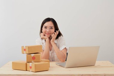 Mutlu Asyalı kadın karton kutuyla ev ambalajlama ve yazma sırası ile çalışıyor, online pazarlama paketleme ve teslimat, KOBİ kavramı