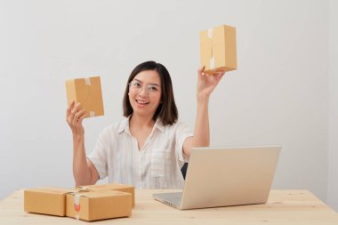 Mutlu Asyalı kadın karton kutuyla ev ambalajlama ve yazma sırası ile çalışıyor, online pazarlama paketleme ve teslimat, KOBİ kavramı