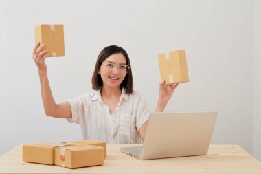 Mutlu Asyalı kadın karton kutuyla ev ambalajlama ve yazma sırası ile çalışıyor, online pazarlama paketleme ve teslimat, KOBİ kavramı