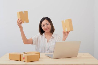 Mutlu Asyalı kadın paket paketleme ve karton kutu ile yazma sırası ile çalışıyor, online pazarlama ve teslimat., 