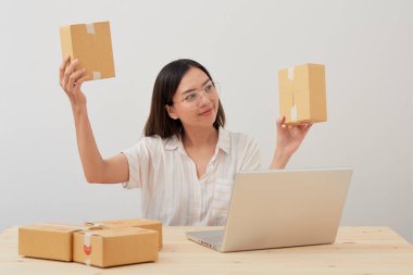 Mutlu Asyalı kadın karton kutuyla ev ambalajlama ve yazma sırası ile çalışıyor, online pazarlama paketleme ve teslimat, KOBİ kavramı
