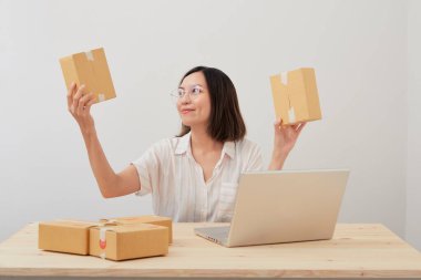 Mutlu Asyalı kadın karton kutuyla ev ambalajlama ve yazma sırası ile çalışıyor, online pazarlama paketleme ve teslimat, KOBİ kavramı