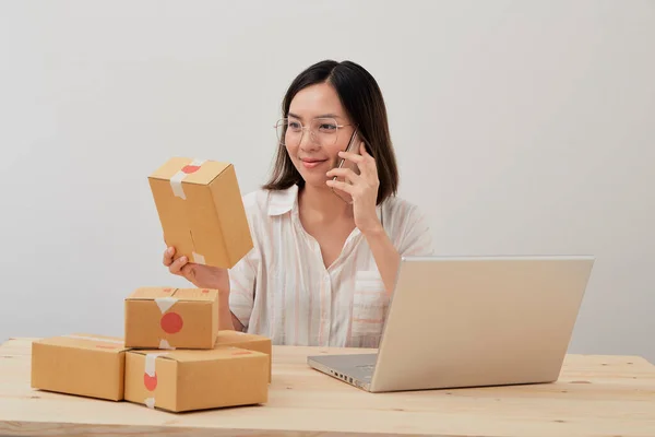Happy asian woman work from home packaging  and writing order with cardboard box , on line marketing packaging and delivery, SME concept