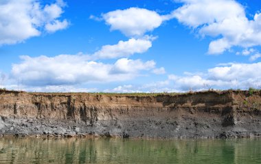 Arka plandaki toprak yüzeyi suyu uzun süre boyunca bir katman olarak görülen kıyı erozyonundan akar..