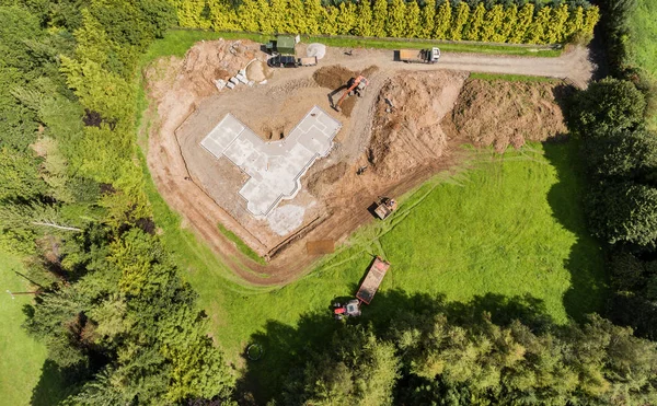 Aves aéreas vista de olhos de uma nova construção de fundação de concreto para uma casa no campo. Campo verde com escavador de máquinas e caminhão basculante e trator . — Fotografia de Stock