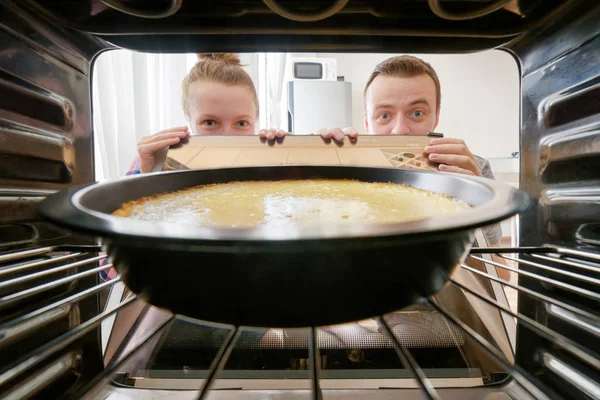 Mujer joven y hombre joven mirando pastel de queso en el horno — Foto de Stock