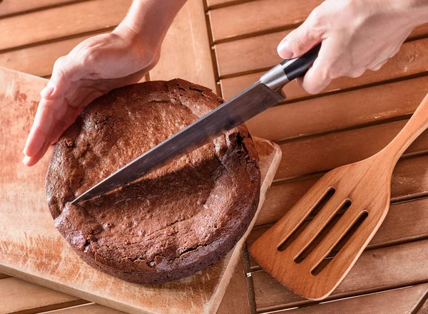 Vista superior da mão segurando faca e corte de bolo de chocolate — Fotografia de Stock