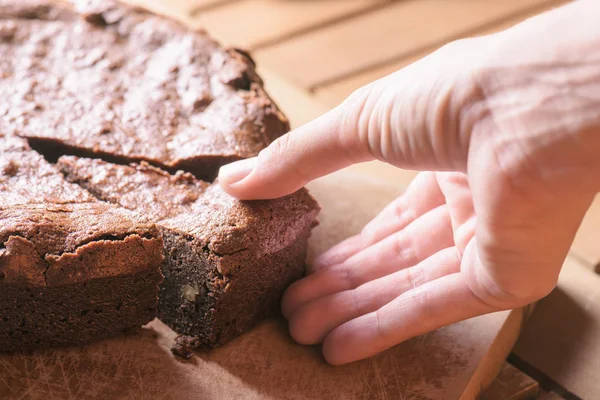 Hand taking piece of freshly baked chocolate brownie cake
