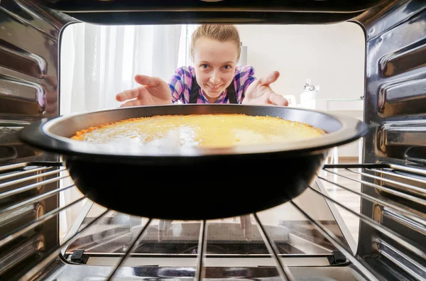 Ung smilende husmor som tar ostekake ut av ovnen på kjøkkenet – stockfoto