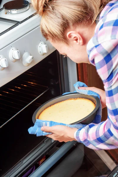 Junge Hausfrau holt Käsekuchen aus Ofen in Küche — Stockfoto