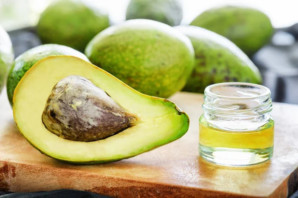 Avocado proaspăt coapte și ulei natural de avocado pe placă de lemn — Fotografie, imagine de stoc