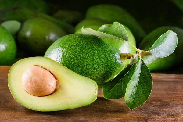 Verse rijpe avocado met groene bladeren op houten tafel — Stockfoto