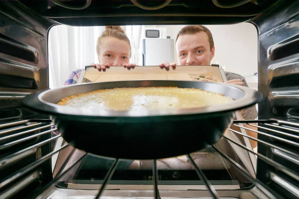 Junge Frau und junger Mann blicken auf Käsekuchen in den Ofen — Stockfoto