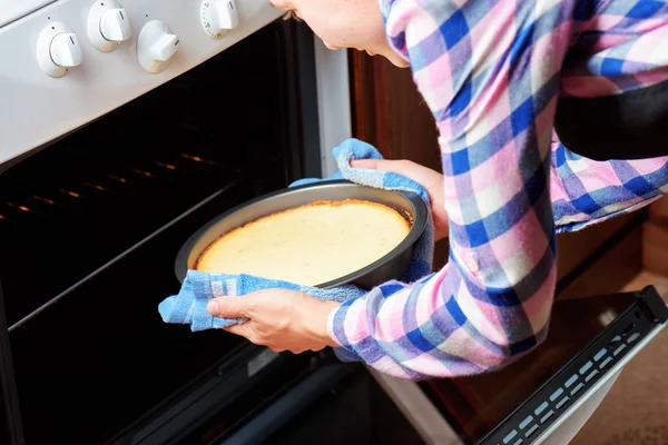 Mujer usando paño de cocina para sacar pastel de queso del horno — Foto de Stock