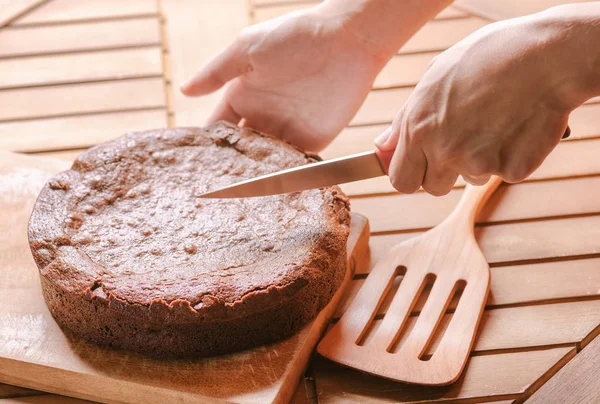 Hand holding knife and cutting freshly baked chocolate brownie — Stock Photo, Image