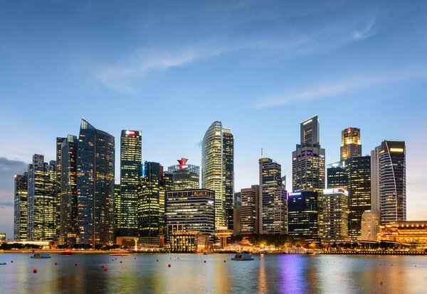 Amazing evening view of downtown in Singapore. Wonderful skyscrapers and other modern buildings are visible on blue sky background. Colorful city lights reflected in water of Marina Bay.