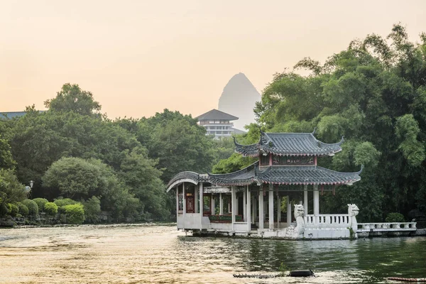 Pavilhão chinês tradicional por lago no parque ao pôr do sol — Fotografia de Stock