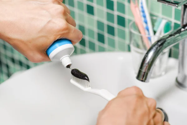 Nahaufnahme der Hände einer Frau, die schwarze Zahnpasta quetscht — Stockfoto