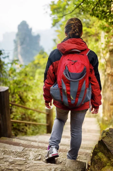 Young female tourist with red backpack descending stone stairs — Stock Photo, Image