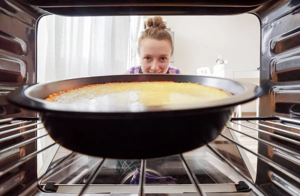 Jovem dona de casa olhando cheesecake no forno — Fotografia de Stock