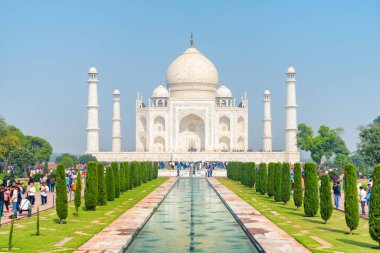 Hindistan 'ın Agra kentindeki Tac Mahal kompleksi boyunca yürüyen bir grup ziyaretçi. Mavi gökyüzü arka planındaki beyaz mermer mozolenin muhteşem manzarası. Muhteşem Babür mimarisi.