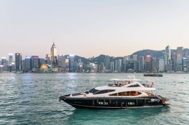 Hong Kong - 21 Ekim 2017 Victoria Limanı 'nda lüks bir yat. Gün batımında Hong Kong Adası ufuk çizgisi. Harika bir şehir manzarası. Hong Kong Asya 'nın popüler bir turistik beldesidir..
