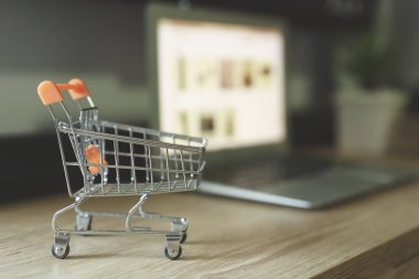 Çevrimiçi alışveriş konsepti, masasında bulanık laptop olan alışveriş arabası.