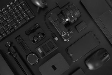 Siyah ofis masasının üstünde bir sürü siyah cihaz dizüstü bilgisayar, dijital kamera, kulaklık, akıllı telefon, harici sabit disk akıllı saat vs..