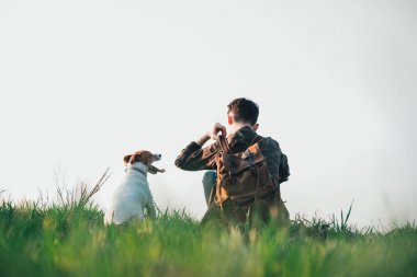 Yeşil çimenlikte küçük beyaz köpekli bir genç.