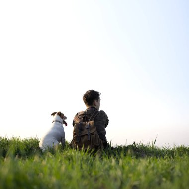 Yeşil çimenlikte küçük beyaz köpekli bir genç.