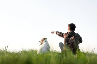 Yeşil çimenlikte küçük beyaz köpekli bir genç.