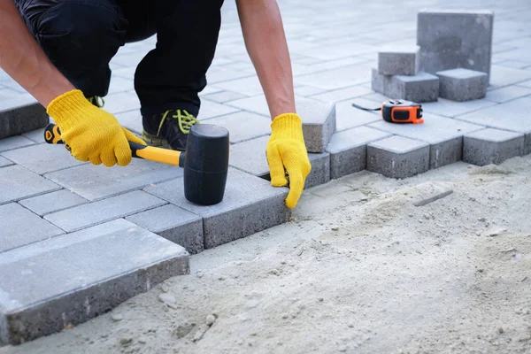 The master in yellow gloves lays paving stones