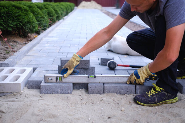 The master in yellow gloves lays paving stones