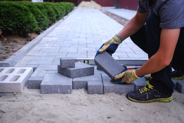 The master in yellow gloves lays paving stones