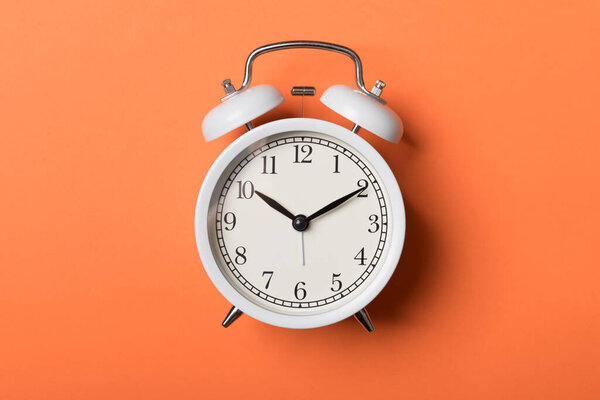 Белый винтажный будильник на оранжевом фоне
