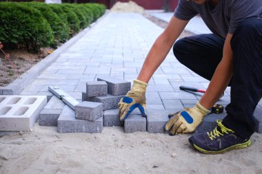 Sarı eldivenli usta kaldırım taşları serer.