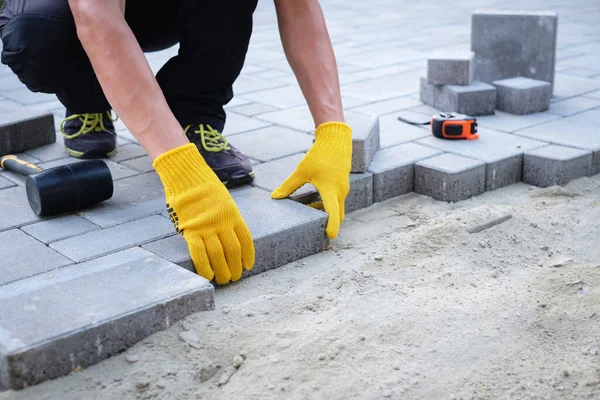 Mistrz w żółtych rękawiczkach układa kostki brukowe — Zdjęcie stockowe