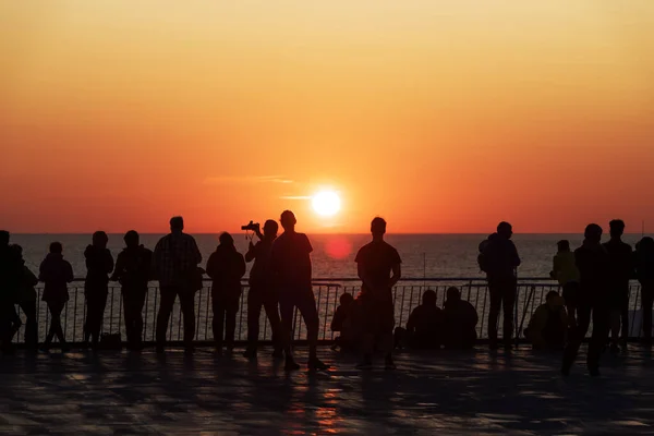 Bir yolcu gemisinin güvertesinde batan güneşe karşı insanların siluetleri. — Stok fotoğraf