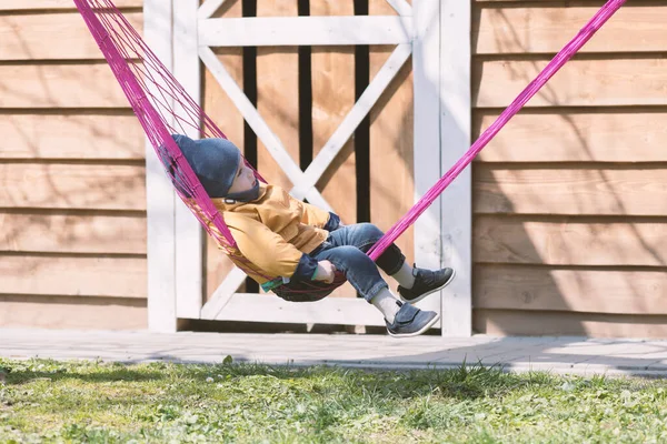 Kleines Kind entspannt sich auf rosa Hängematte im Frühlingsgarten — Stockfoto