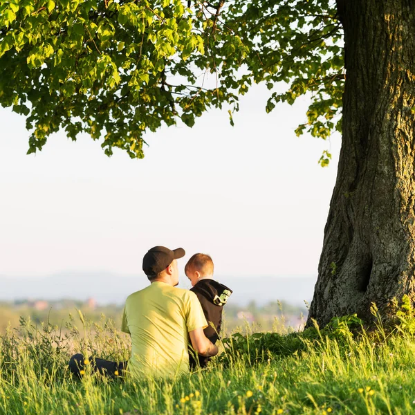 Papá con hijo en el prado de primavera sentado debajo del árbol —  Fotos de Stock