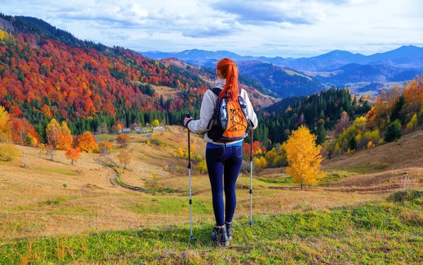 Uma menina de esportes com uma mochila e paus turísticos observa as montanhas . — Fotografia de Stock