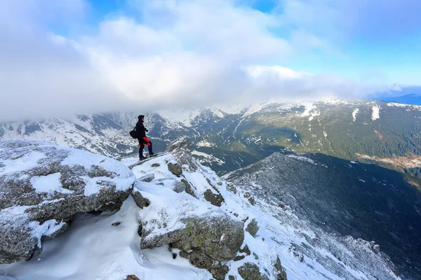 Homem barbudo com uma bolsa em seu ombro fica em uma rocha e contempla os picos de montanha cobertos de neve . — Fotografia de Stock