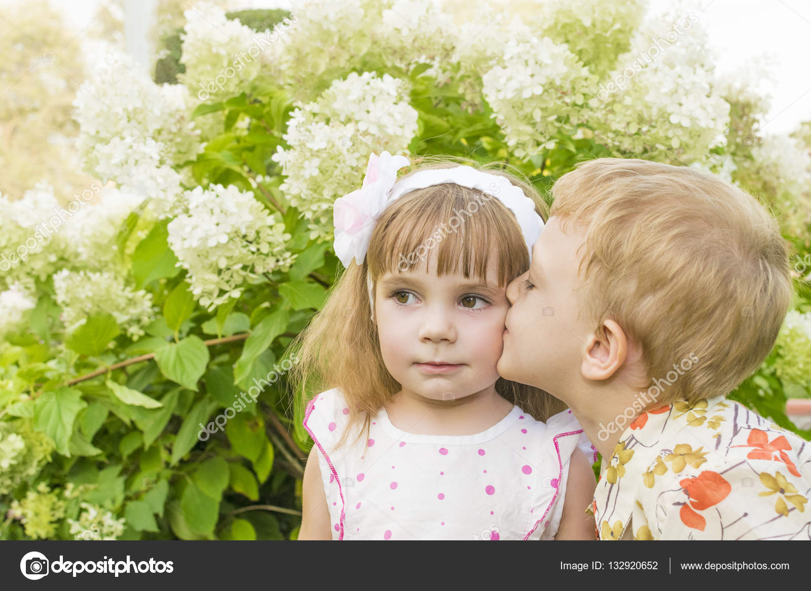Little boy kissing a girl in beautiful flower bushes — Stock Photo