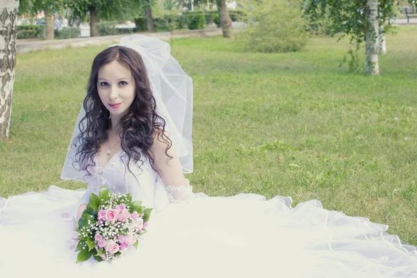 Szép, boldog menyasszony egy esküvői ruha ül a fűben, a parkban — Stock Fotó