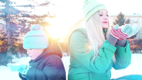 Glad lille sød baby og mor på en solrig vinterdag leger med sneen og blæser sne på – Stock-video
