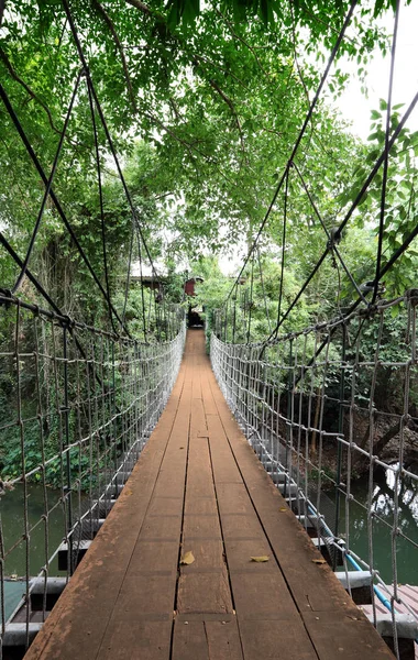 Ponte sospeso verticale in legno attraversano un piccolo fiume per ospitare . — Foto Stock