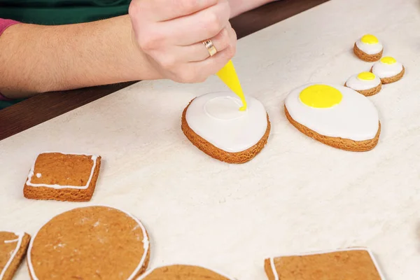 Drawing yolk on gingerbread shaped as an egg and coated with white glaze